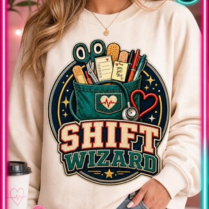 May include: Cream-colored sweatshirt featuring a graphic of a medical kit with scissors, bandages, pens, and the text "SHIFT WIZARD." A stethoscope and heart shape are also included in the design. The sweatshirt is a casual style.