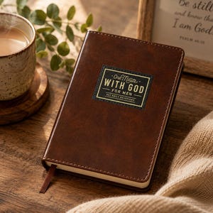 May include: A dark brown, leather-textured devotional book with a rectangular black label on the front cover. The label features gold text that reads One Minute WITH GOD FOR MEN 365 DAILY DEVOTIONS. A thin brown ribbon bookmark extends from the bottom.