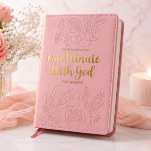 May include: A pink devotional book titled One Minute With God For Women, featuring gold foil lettering and embossed rose floral patterns on the cover. The book has a stitched edge and a small pink ribbon bookmark extending from the bottom corner.