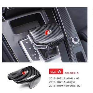 Może przedstawiać: Osłona dźwigni zmiany biegów z włókna węglowego z czerwonym i białym logo "S". Zaprojektowana dla modeli Audi, w tym 4L/A5, Q5L i Q7. Obraz przedstawia osłonę zamontowaną we wnętrzu samochodu, obok dźwigni zmiany biegów.