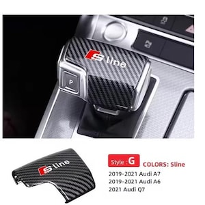 Può includere: Copertura del cambio in stile fibra di carbonio con il logo S line in rosso e bianco. Progettato per i modelli Audi A7, A6 e Q7. L'immagine mostra anche la leva del cambio e la console circostante.