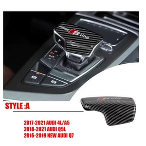 May include: Carbon fibre gear shift knob cover featuring the S line logo in red. The cover is designed for Audi models, including the 4L/A5, Q5L, and Q7. The image also shows the car's interior with the gear shift and other controls.