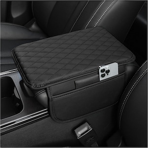 May include: Black car armrest cover with a quilted diamond pattern. The cover has a pocket with a smartphone inside. The armrest is installed in a car with black leather seats and white stitching.