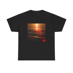 May include: Black t-shirt with a square graphic depicting a sunset over water. The graphic has orange, red, and yellow tones. The text "Better Than Words" is printed on the graphic, along with the names "Ronnie Santos" and "Prince Royce".