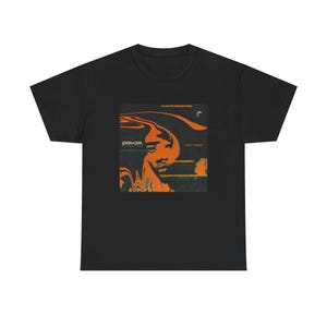 May include: Black t-shirt featuring a graphic design with an orange and black portrait and the text "Leon Thomas". The design has a retro, psychedelic style. The shirt is made of a soft material.