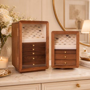 May include: Two wooden jewelry organizers with glass fronts and brass-toned knobs. The larger unit features five drawers and a top ring display section, while the smaller unit has three drawers and a top ring display section, both lined in white.
