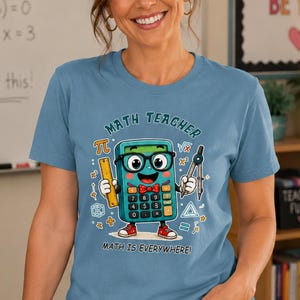 Könnte beinhalten: Ein staubblaues T-Shirt mit einer Cartoon-Taschenrechner-Figur, die eine schwarze Brille und eine rote Fliege trägt. Der Taschenrechner hält ein gelbes Lineal und einen Zirkel. Der Text lautet MATH TEACHER und MATH IS EVERYWHERE.