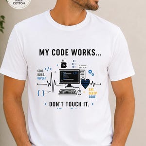 May include: A white short-sleeved t-shirt featuring a graphic print with the text MY CODE WORKS... DON'T TOUCH IT. The design includes a computer monitor, keyboard, coffee mug, heart, and binary code elements in black, blue, and yellow colours.
