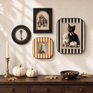 May include: A gallery wall arrangement featuring four framed art pieces: a round frame with a skeleton key, a rectangular black frame with an arched sketch of a house, a square orange and white striped frame with a ghost, and a black and white striped frame with a black kitten. Below are two white pumpkins, a brass candlestick, and a wooden bowl with acorns.