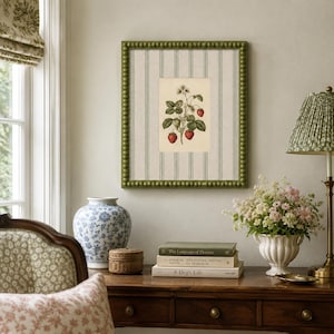 May include: A square wall art piece featuring a botanical illustration of a strawberry plant with red berries and green leaves, centered on a cream-colored background with vertical sage green stripes, enclosed in a beaded olive green frame.