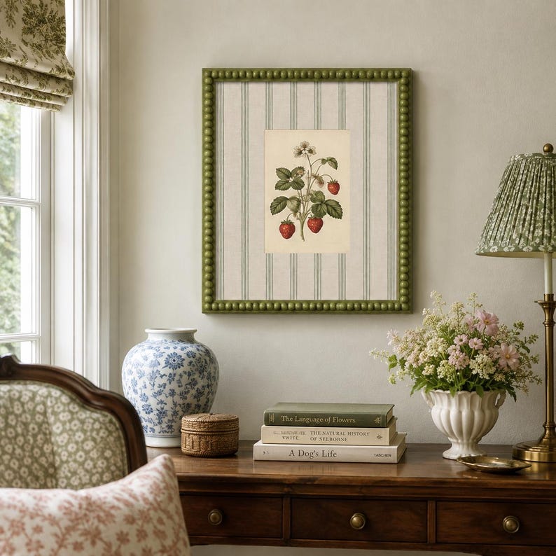 May include: A square wall art piece featuring a botanical illustration of a strawberry plant with red berries and green leaves, centered on a cream-colored background with vertical sage green stripes, enclosed in a beaded olive green frame.