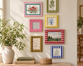 May include: A collection of seven rectangular picture frames with varied patterns and colors, including stripes, dots, and solid textures, arranged on a wall. The frames contain botanical prints, landscape art, and patterned paper inserts.