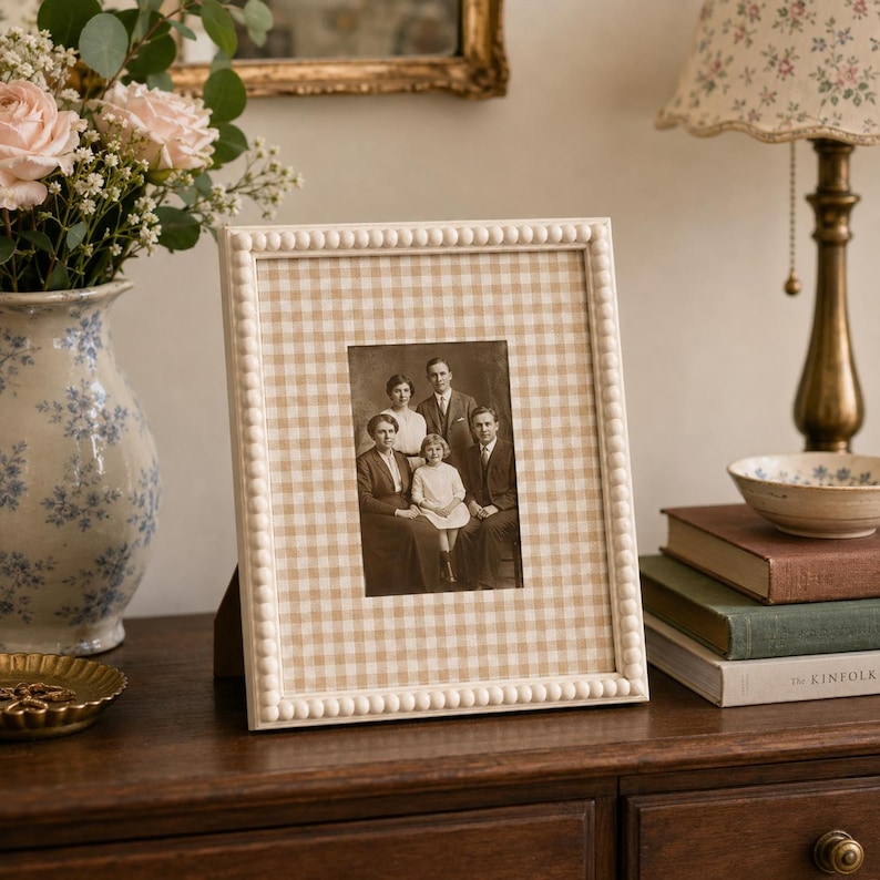 May include: A rectangular picture frame with a white beaded border and a light tan and white gingham patterned mat. The frame holds a black and white vintage photograph of a family of four, including two adults and two children.