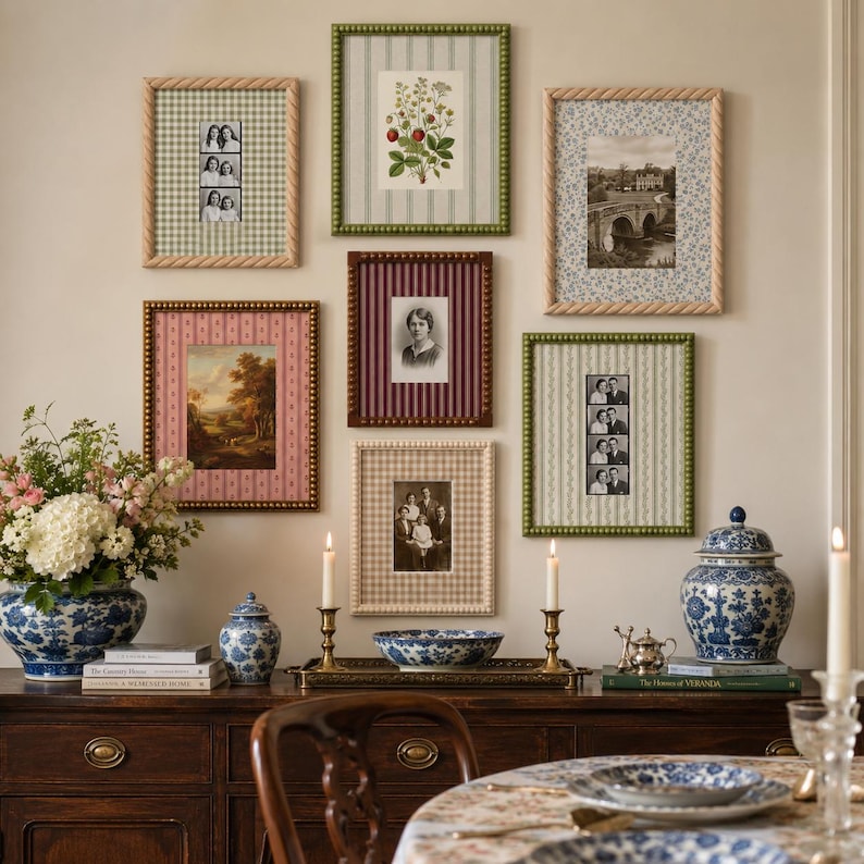 May include: A gallery wall featuring six rectangular picture frames with varied patterned mats and beaded or rope-style borders, displaying black and white photographs and a botanical print, arranged above a dark wood sideboard with blue and white decor.