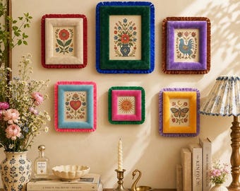 May include: A collection of six rectangular wall frames with colorful velvet borders, each containing a botanical or folk art print. The frames feature vibrant red, blue, green, purple, pink, and yellow velvet edges with ruffled trim.