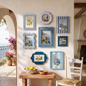 Puede incluir: Una composición de pared con ocho marcos de fotos variados en tonos azul y blanco, que muestran láminas costeras y botánicas. Debajo, una mesa de madera sostiene un cuenco de cerámica lleno de limones amarillos y un cuenco de madera.
