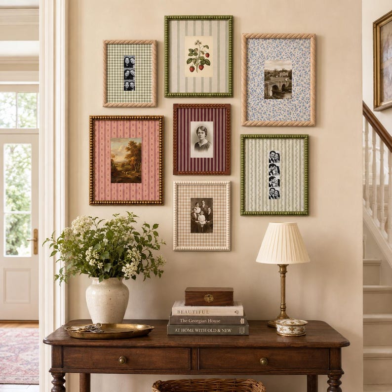 May include: A gallery wall arrangement featuring seven rectangular picture frames with varied patterned mats and beaded borders, displaying botanical art, black and white photographs, and landscape prints, mounted above a wooden console table.