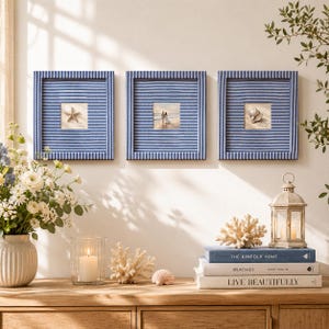 May include: Three square framed pictures with blue and white striped borders. Each frame contains a different image: a starfish, a couple walking on a beach, and a seashell. The frames are displayed above a wooden surface with decorative items.