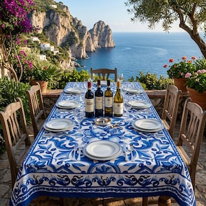 May include: A table set for dining with a blue and white floral tablecloth, white plates, and wine glasses. Several bottles of wine are on the table. Wooden chairs surround the table, with a scenic ocean view in the background.