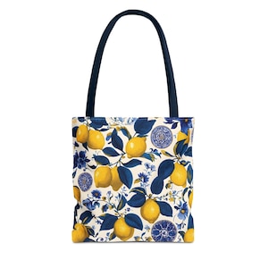 May include: Tote bag with a lemon and floral pattern. The bag features a cream-coloured background with yellow lemons, blue leaves, and blue floral accents. It has a navy blue handle.