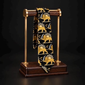May include: A black necktie featuring a repeating gold-coloured pattern of a lion holding a sword beneath a rising sun. The tie is draped over a horizontal wooden bar supported by two vertical gold-coloured metal posts on a rectangular wooden base.