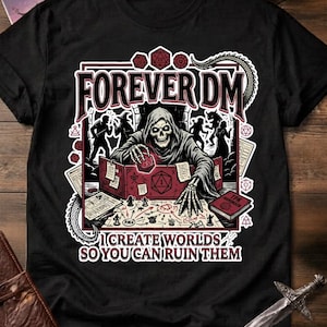 Könnte beinhalten: Schwarzes T-Shirt mit einer Grafik, die einen Kapuzenskellett, Würfel und den Text "FOREVER DM" zeigt. Das Design enthält den Satz "I CREATE WORLDS SO YOU CAN RUIN THEM". Das Shirt wird auf einer Holzoberfläche präsentiert.