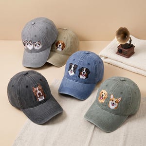 Op de afbeelding: Vijf baseballpetten in diverse kleuren, waaronder grijs, beige, blauw, donkergrijs en olijfgroen. Elke pet is voorzien van geborduurde dierenportretten, waaronder katten op de grijze pet en verschillende hondenrassen op de andere vier petten.