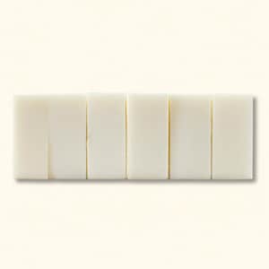 May include: Six rectangular bars of white soap are arranged horizontally against a cream-colored background. The bars are evenly spaced and have a smooth, clean appearance, suggesting a focus on natural ingredients and personal care.