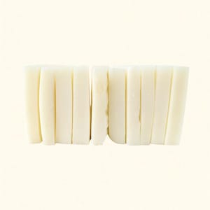 May include: A close-up shot of a stack of white, rectangular food items. The items are arranged vertically, side by side, creating a textured surface. The food items appear to be a type of rice cake or similar food product.