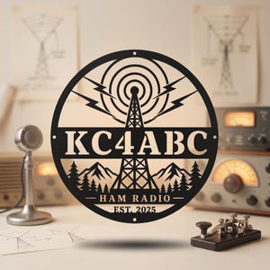 Puede incluir: Letrero metálico negro con un diseño circular que presenta una torre de radio, rayos y el texto "KC4ABC - HAM RADIO - EST. 2025". El letrero también incluye una silueta de montaña y bosque.