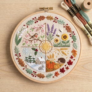 Peut inclure: Un cercle à broder rond avec un motif détaillé représentant les quatre saisons. Le motif comprend un oiseau, des fleurs, une abeille, des citrouilles et une scène d'hiver. Des fils à broder de différentes couleurs sont à proximité.