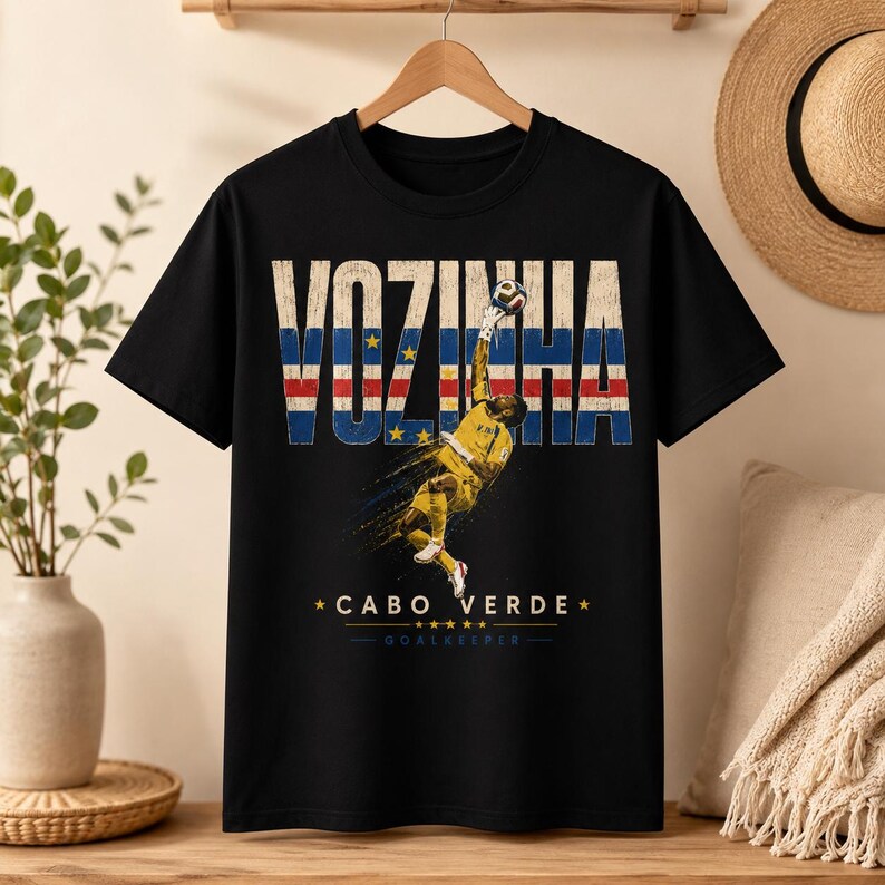 Może przedstawiać: Czarny t-shirt z kr&oacute;tkim rękawem z grafiką bramkarza w ż&oacute;łtym stroju skaczącego do piłki nożnej. Napis VOZINHA jest wydrukowany dużymi literami wypełnionymi wzorem flagi Republiki Zielonego Przylądka, a poniżej znajduje się napis CABO VERDE GOALKEEPER.