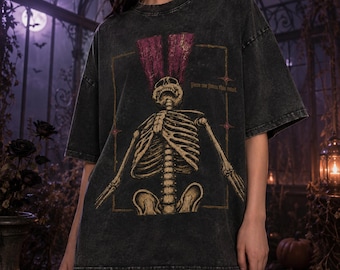 May include: A charcoal grey acid-wash t-shirt featuring a graphic of a skeleton with its head tilted back and purple flame-like shapes rising from its skull. The design includes the text "Free me from this mind" in a thin, gold-colored font.