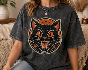 May include: A charcoal grey acid-wash t-shirt featuring a circular graphic of a black cat with wide orange eyes and an open mouth showing teeth. The design includes orange lightning bolt accents and a star symbol set against a circular orange background.