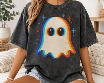 May include: A charcoal grey acid-wash t-shirt featuring a central graphic of a white ghost with large black eyes. The ghost is outlined in a vibrant rainbow-colored border with a glitch effect, surrounded by small multi-colored four-pointed stars.