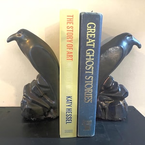 Può includere: Due fermalibri a forma di uccello color bronzo scuro, raffiguranti corvi appollaiati su basi rocciose, che fiancheggiano due libri. Il libro a sinistra è giallo con il testo THE STORY OF ART di KATY HESSEL, quello a destra è blu con il testo GREAT GHOST STORIES.