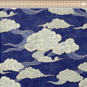 Könnte beinhalten: Marineblauer Stoff mit einem sich wiederholenden Muster aus stilisierten weißen Wolken und fließendem Wasser. Die Wolken haben ein strukturiertes Aussehen, und das Wasser hat ein wellenartiges Design. Das Design erinnert an traditionelle asiatische Kunst.