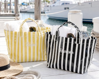 May include: Two rectangular tote bags with vertical stripes, one in yellow and white and the other in black and white. Each bag features two top handles, a white towel inside, and a name embroidered on the front: Reese on the yellow bag and Harper on the black bag.