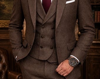 May include: A three-piece brown suit with a white dress shirt and a burgundy tie. The suit features a notched lapel jacket, a double-breasted vest, and matching trousers. A silver wristwatch is visible on the wrist.