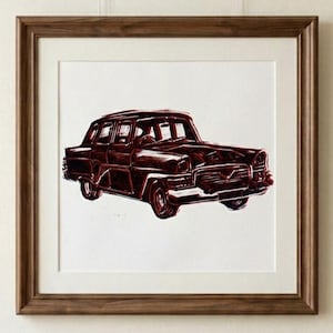Puede incluir: Una impresión enmarcada con una ilustración de un coche antiguo en burdeos y blanco. La obra de arte representa un sedán clásico con líneas detalladas, sobre un fondo blanco, en un marco de madera marrón.