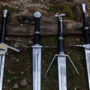 May include: Four metal swords with black grips arranged side by side. The first sword features a circular gold-toned guard, the second has a round pommel, the third includes a stylized animal-shaped crossguard, and the fourth has a twisted guard.