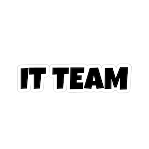 Könnte beinhalten: Ein weißer Aufkleber mit dem Text "IT TEAM" in fetten, schwarzen Buchstaben. Die Buchstaben haben einen leichten Schatteneffekt, und der Aufkleber hat einen weißen Rand. Der Text ist zentriert.