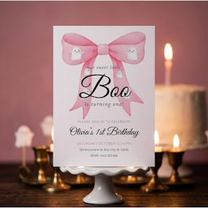 May include: A white rectangular birthday invitation card featuring a large pink watercolour bow with small white ghost illustrations. The text reads: our sweet little Boo is turning one! PLEASE JOIN US TO CELEBRATE Olivia's 1st Birthday SATURDAY | OCTOBER 12 | 4 PM 123 Anywhere St. Any City St. 12345 RSVP: 0412 123 456.