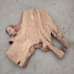 Peut inclure: Une dalle de bois naturelle de couleur brun clair, avec des motifs de grain visibles. La dalle a une forme irrégulière avec un trou et une surface texturée, idéale pour un élément de décoration rustique.