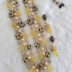 May include: A multi-strand necklace and earring set. The necklace features yellow, pearl, and rhinestone beads with ornate gold-toned accents. The earrings have a matching design with yellow gemstone drops. The jewelry is displayed on a white surface.
