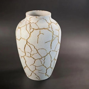 May include: A white ceramic vase with a crackle pattern filled with gold-colored accents. The vase has a rounded body and a slightly flared opening, suitable for home decor.