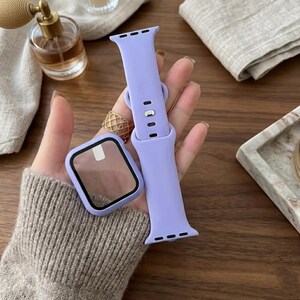 May include: A lilac watch strap and protective case. The watch strap is made of a soft, flexible material and has a classic design. The protective case has a clear screen protector. The items are displayed on a wooden surface.