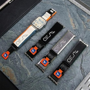 May include: Four Apple Watch bands in various colors: white and orange, black, gray, and dark gray. Each band features a black buckle, orange accents, and the word "CRAFT". The watch displays the time 10:09.