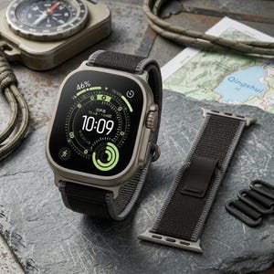 May include: A smartwatch with a black and gray fabric band, displaying the time as 10:09. The watch face shows a green and white interface with various data points. An additional watch band and a compass are also visible.