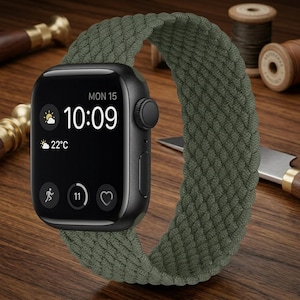 May include: A black smartwatch with a rectangular screen displaying the time 10:09, the date Monday 15, weather icons, and activity metrics. The watch features a textured, olive green braided elastic band that forms a continuous loop.
